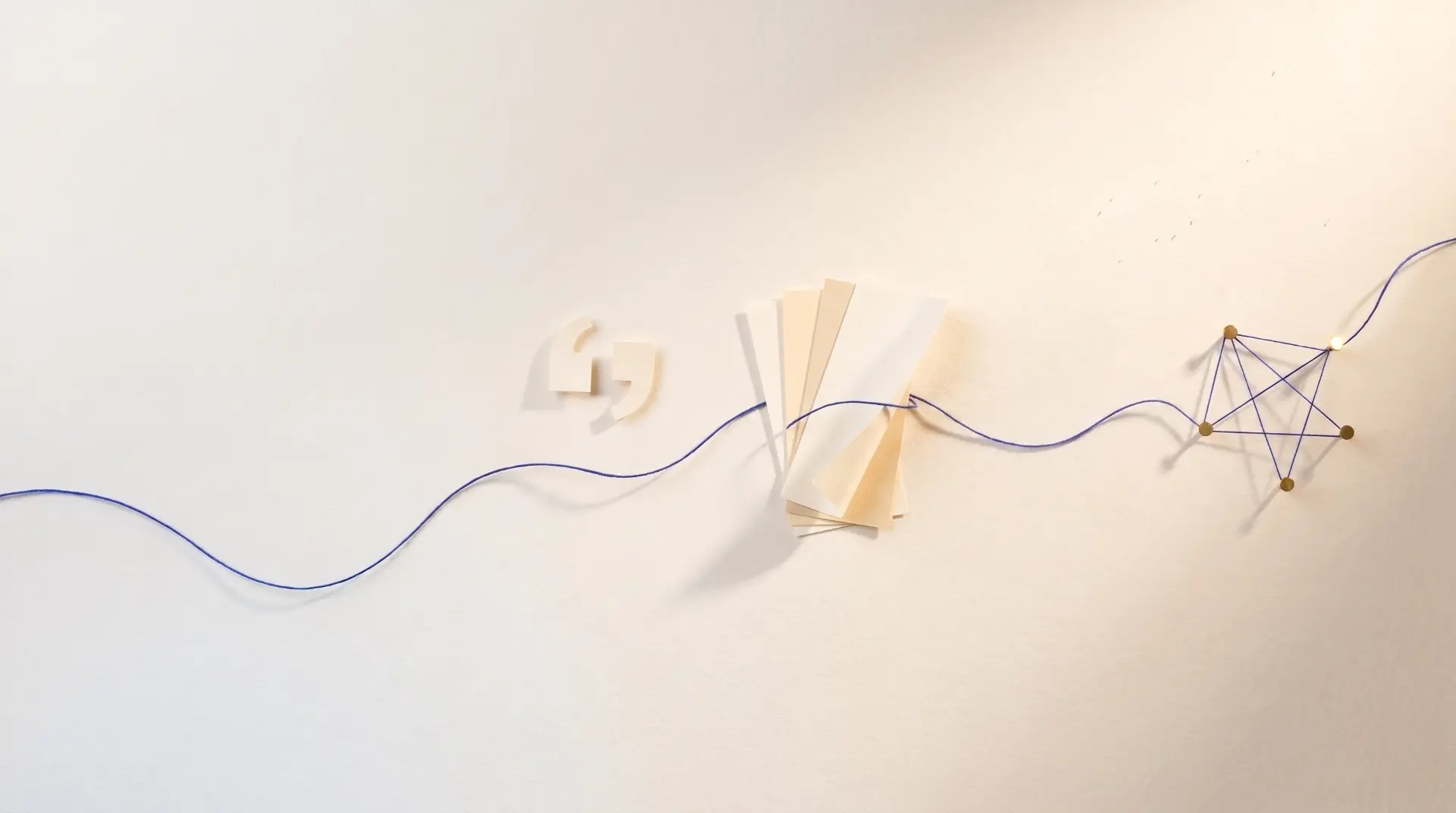 Ein blauer Faden verläuft über eine helle Papierfläche, führt durch einen Fächer aus Papierstreifen und endet rechts in einer Konstellation aus goldenen Punkten, die durch Fäden verbunden sind.